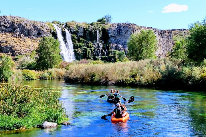 Kayakers on a river with a waterfall and rocky cliffs in the background.