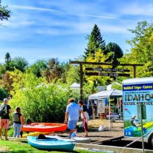 People near kayaks and Idaho guide service trailer at Ritter Island, surrounded by trees.