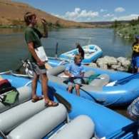 People with inflatable rafts by a river under a clear blue sky.