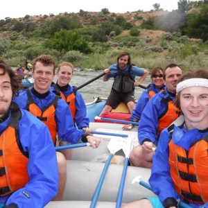 Group of people in blue jackets and orange life vests rafting on a river.