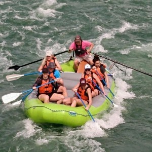 Group of people rafting in a green inflatable boat on rough water.