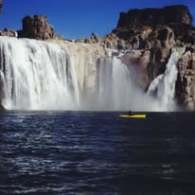 Kayaker in yellow kayak paddling near large waterfall under clear blue sky