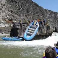 Raft stuck on rocks with people surrounding it near a river.