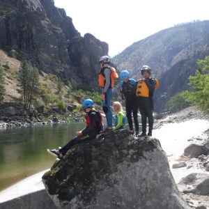 Group of people in helmets and life jackets by a river in a rocky canyon.