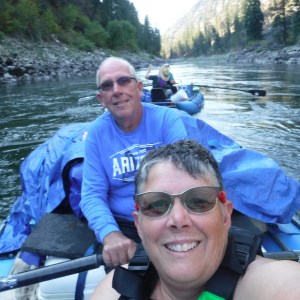 Two people in a raft on a scenic river with forested banks.