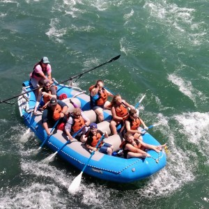 Group of people whitewater rafting in a blue inflatable raft wearing life jackets.